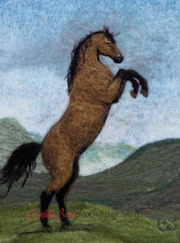 artwork wool painting of a brown horse with black mane and tail rearing on its hind legs on a hillside pasture of green grass with mountains and blue skies in the background. 