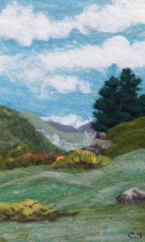 artwork painting made from wool of a mountain landscape with green grass and trees, stones and a blue sky with clouds.